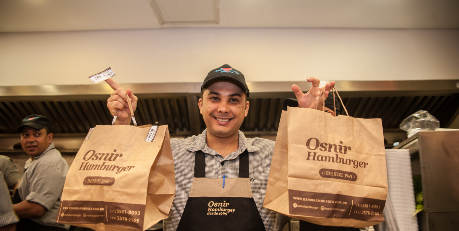 Entregador da Osnir Hamburger segurando sacolas de pedidos na cozinha